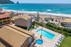 A hotel with a swimming pool, beach view, and a mountainous backdrop.