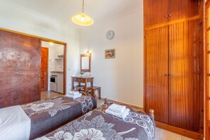 A hotel room with two beds, a wooden wardrobe, a desk with a mirror, and a clock on the wall.