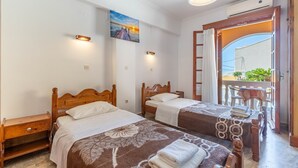 Ein Schlafzimmer mit zwei Holzbetten, einem Nachttisch, einem Gemälde an der Wand und einem Balkon mit Tisch und Stühlen.