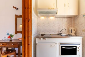 Una cocina compacta con estufa, horno y lavaplatos, una mesa de madera con un florero y una botella, y un espejo en la pared.