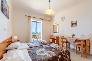 Habitación de hotel con dos camas, un escritorio, una silla, una mesa, un balcón con vistas y un reloj en la pared.