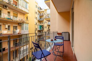 Un balcon avec deux chaises et une petite table, donnant sur une cour intérieure bordée de plusieurs bâtiments.