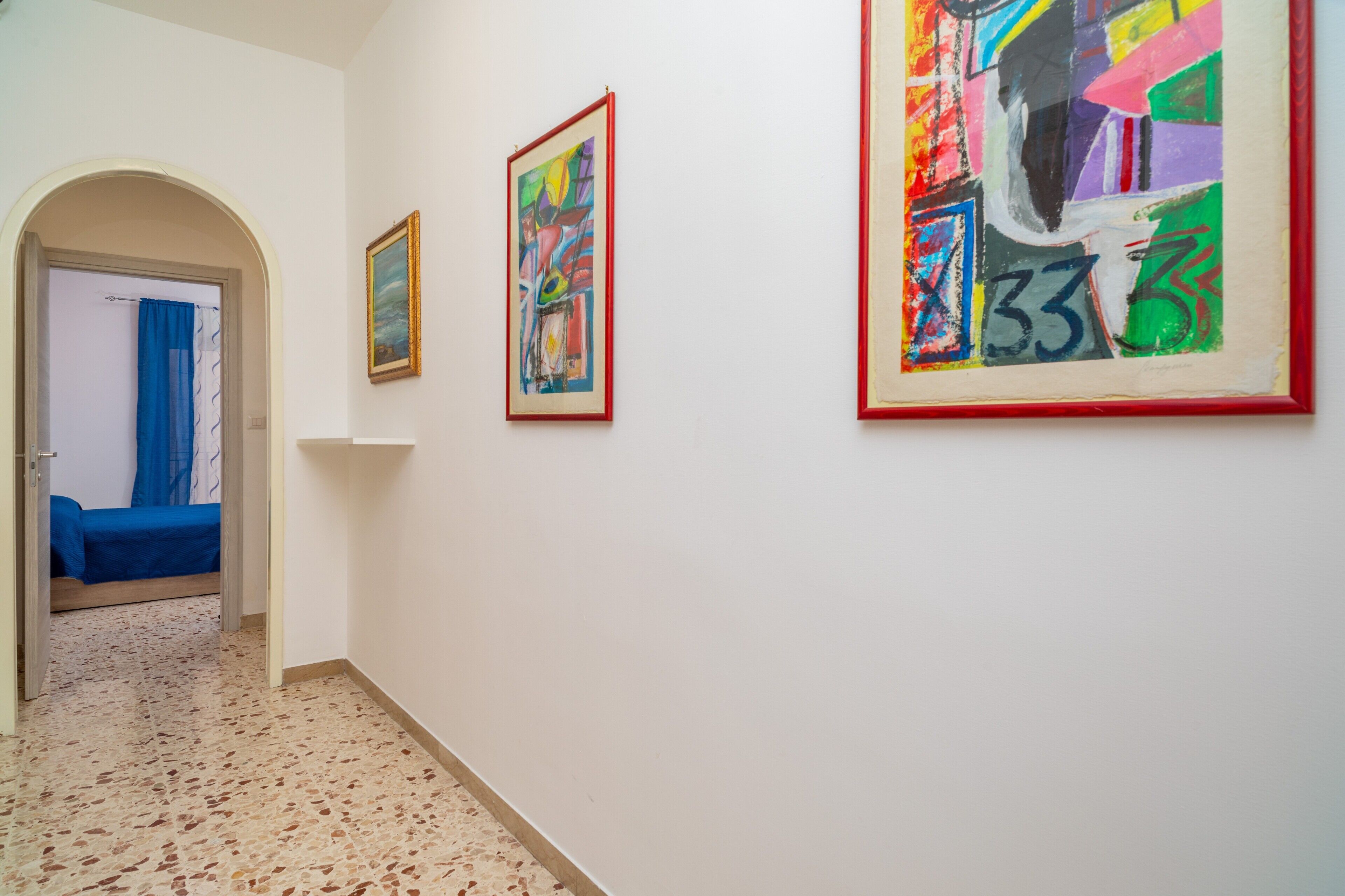 A hallway with a bed, a door, and three framed artworks on the wall.