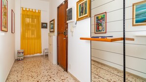Un pasillo con suelo de baldosas, una puerta de madera, una cortina amarilla y un teléfono fijo en la pared.