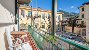 Un balcon avec une table et des chaises, une vue sur des immeubles et une rue bordée de voitures garées.