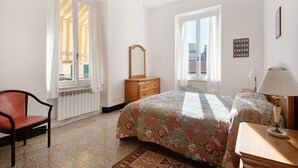 Une chambre à coucher avec un lit, une chaise, une commode, un miroir, une fenêtre et une lampe.