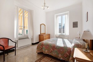 Une chambre à coucher avec un lit, une chaise, une commode, un miroir, une fenêtre et une lampe.
