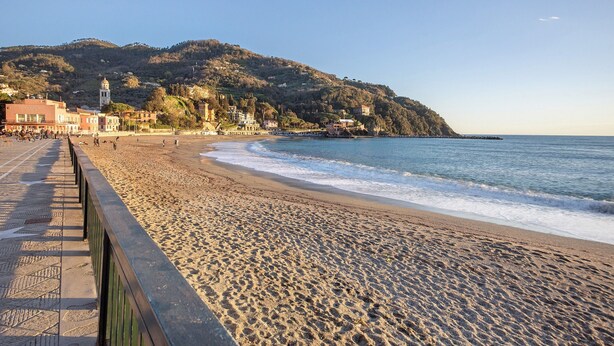 Une plage avec une promenade, une ville côtière et une colline surmontée d’une tour.