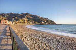 A beach with a promenade, a coastal town, and a hill with a tower.