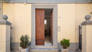 Une entrée d’immeuble avec une porte en bois, des plantes en pot et un panneau indiquant le numéro de l’immeuble.