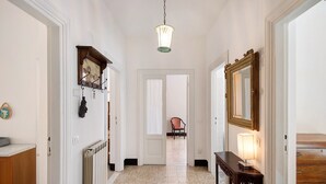 Un couloir avec un radiateur, un luminaire suspendu, un miroir et une chaise au fond.