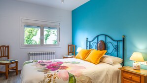 Une chambre à coucher avec un lit, une fenêtre, une chaise, une table de chevet et une lampe.