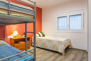 Ein Schlafraum mit Etagenbetten, einem Fenster, einem Nachttisch mit Lampe und einem Bett mit Blumenmuster-Überwurf.