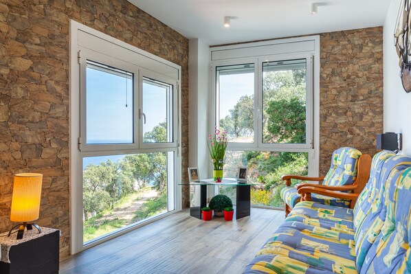 Ein Zimmer mit Stewand, großen Fenstern, einer Couch, einem Tisch und einer Lampe.