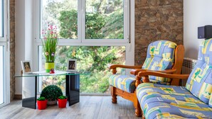 Une pièce avec une chaise en bois, une table en verre et une vue sur la verdure par une grande fenêtre.