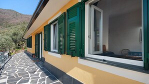 A building with a stone-tiled balcony, green shutters, and a mountain backdrop. - Apartment 'Ca' Dû Massunin' with Sea View, Wi-Fi and Air Conditioning (Recco)