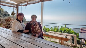 Two people seated at a wooden table with a view of the sea and greenery in the background. - Apartment 'Ca' Dû Massunin' with Sea View, Wi-Fi and Air Conditioning (Recco)