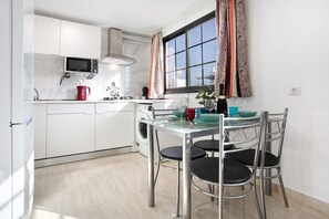 Une cuisine moderne avec des meubles blancs, un four à micro-ondes, une machine à café et un coin repas comprenant une table en verre et des chaises en métal.