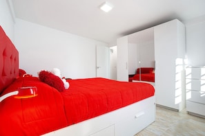 Une chambre à coucher moderne avec une couvre-lit rouge, une armoire blanche et un miroir.