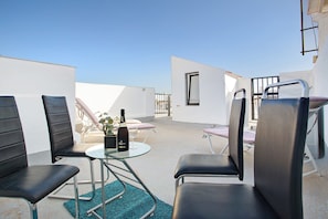 Une terrasse sur le toit, avec des fauteuils en cuir noir, une table en verre, une bouteille de champagne et une plante en pot.
