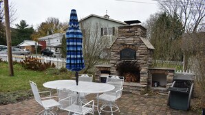 A patio with a stone fireplace, white metal chairs, and a blue umbrella.