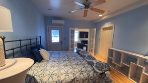 A bedroom with a bed, a ceiling fan, a door leading to another room, and a window.