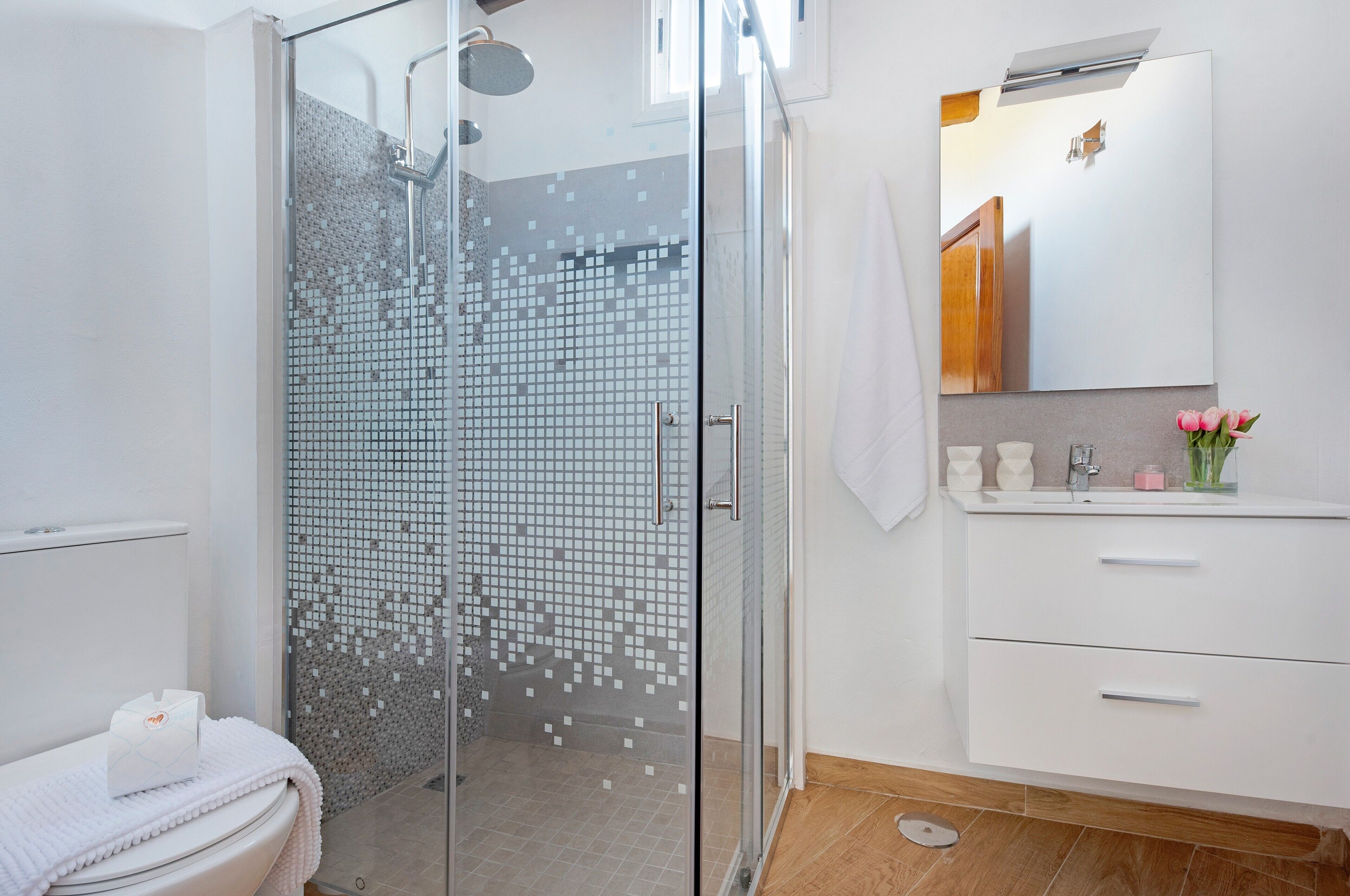 Un baño moderno con cabina de ducha de vidrio, tocador blanco con espejo y inodoro con toalla.