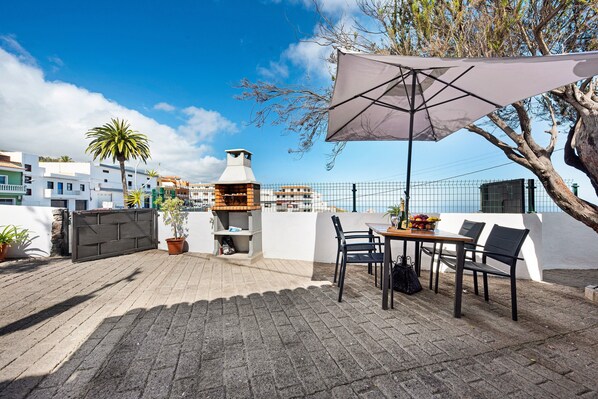 Une terrasse avec une table et des chaises, un barbecue et une plante en pot.