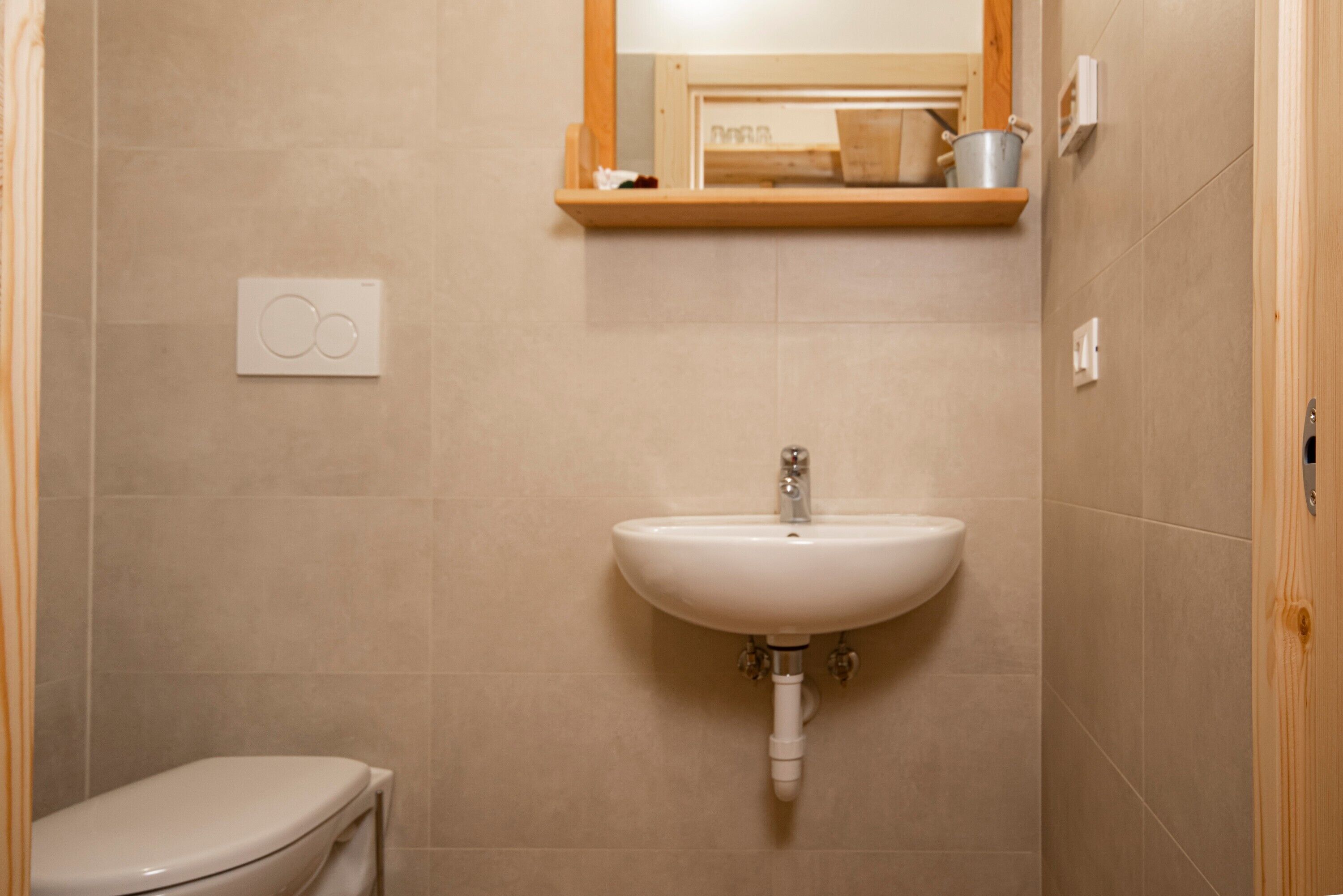 Ein Badezimmer mit einem weißen Waschbecken, einer Toilette und einem Holzregal darüber.