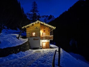 A log cabin with a balcony, surrounded by snow, at night.