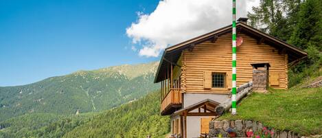 A log cabin with a balcony, outdoor seating, and a mountain view.