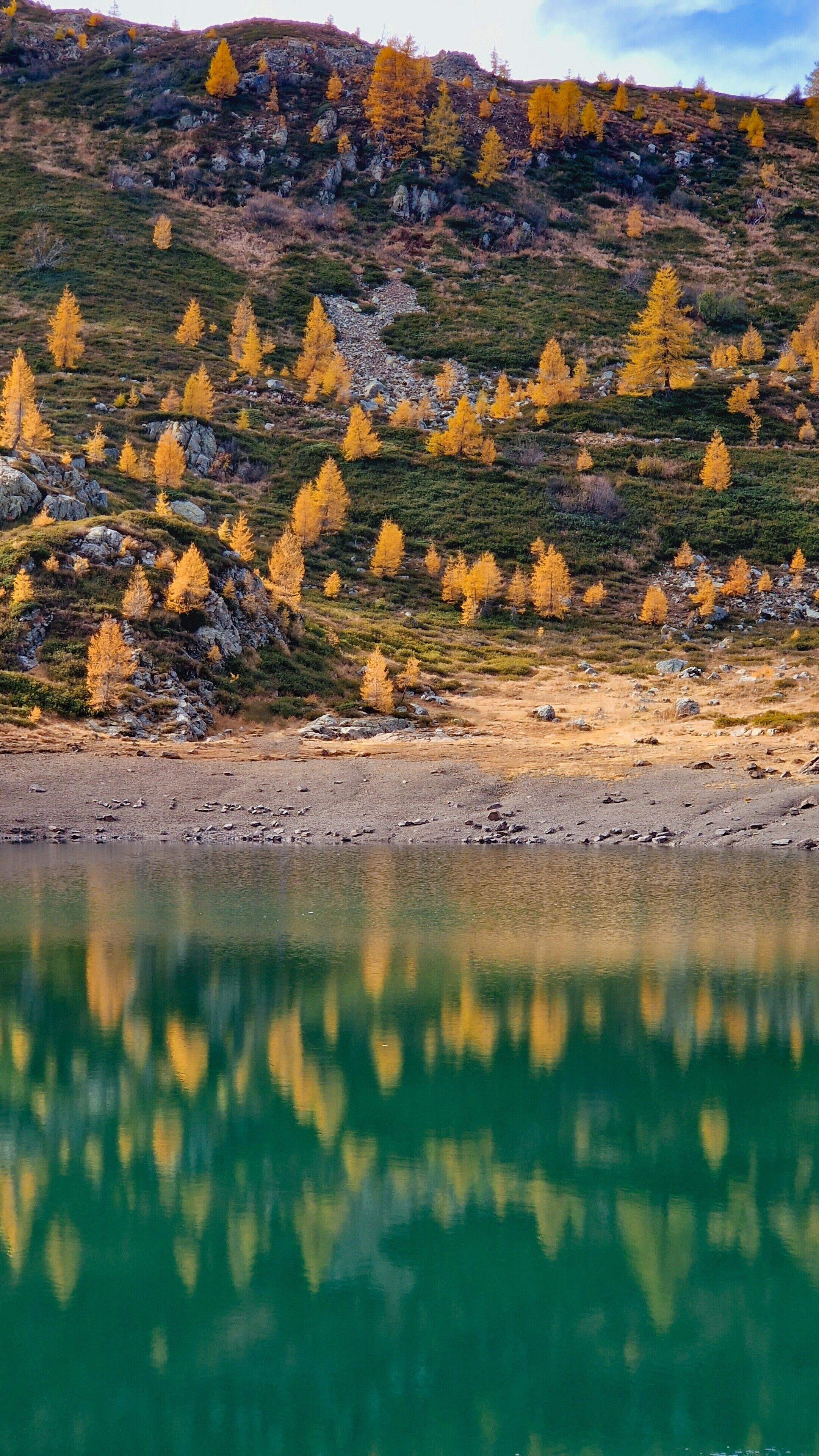 Un paysage naturel avec une étendue d’eau reflétant les arbres, une colline rocheuse et un ciel dégagé.