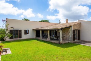 A house with a covered patio, a lawn, and a stone wall.