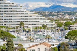 A marina with numerous boats, a large hotel building, and a mountainous backdrop.