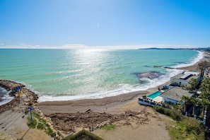 A coastal view with a beach, ocean, and a row of houses with a swimming pool.