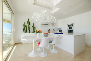 A modern kitchen with white cabinetry, a central island, and a dining area with white chairs.
