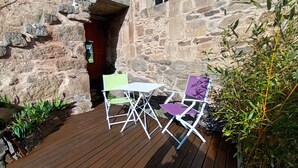 Una terraza de madera con un muro de piedra, dos sillas y una mesa.