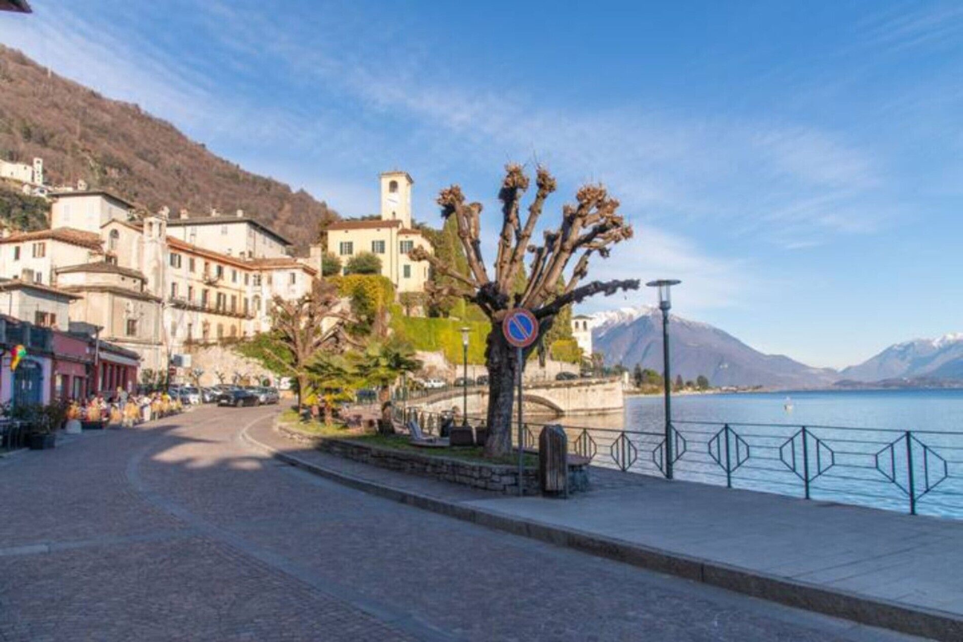 A cobblestone street with buildings, a no parking sign, and a body of water with mountains in the background.