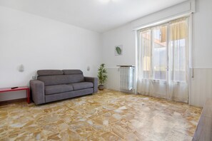 Un salon avec un canapé gris, une petite table, une plante en pot et une porte-fenêtre coulissante.
