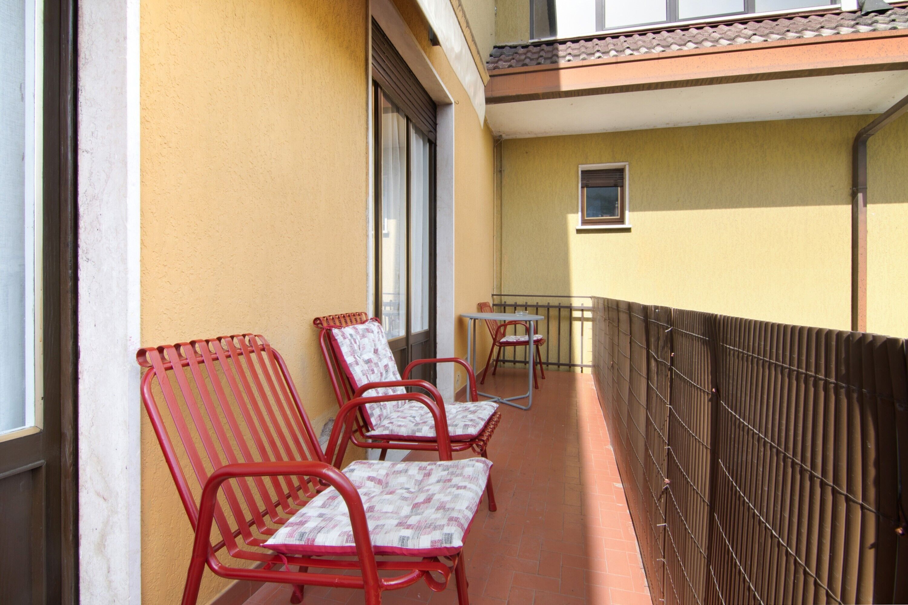 A balcony with red metal chairs and a small table, a window, and a door.