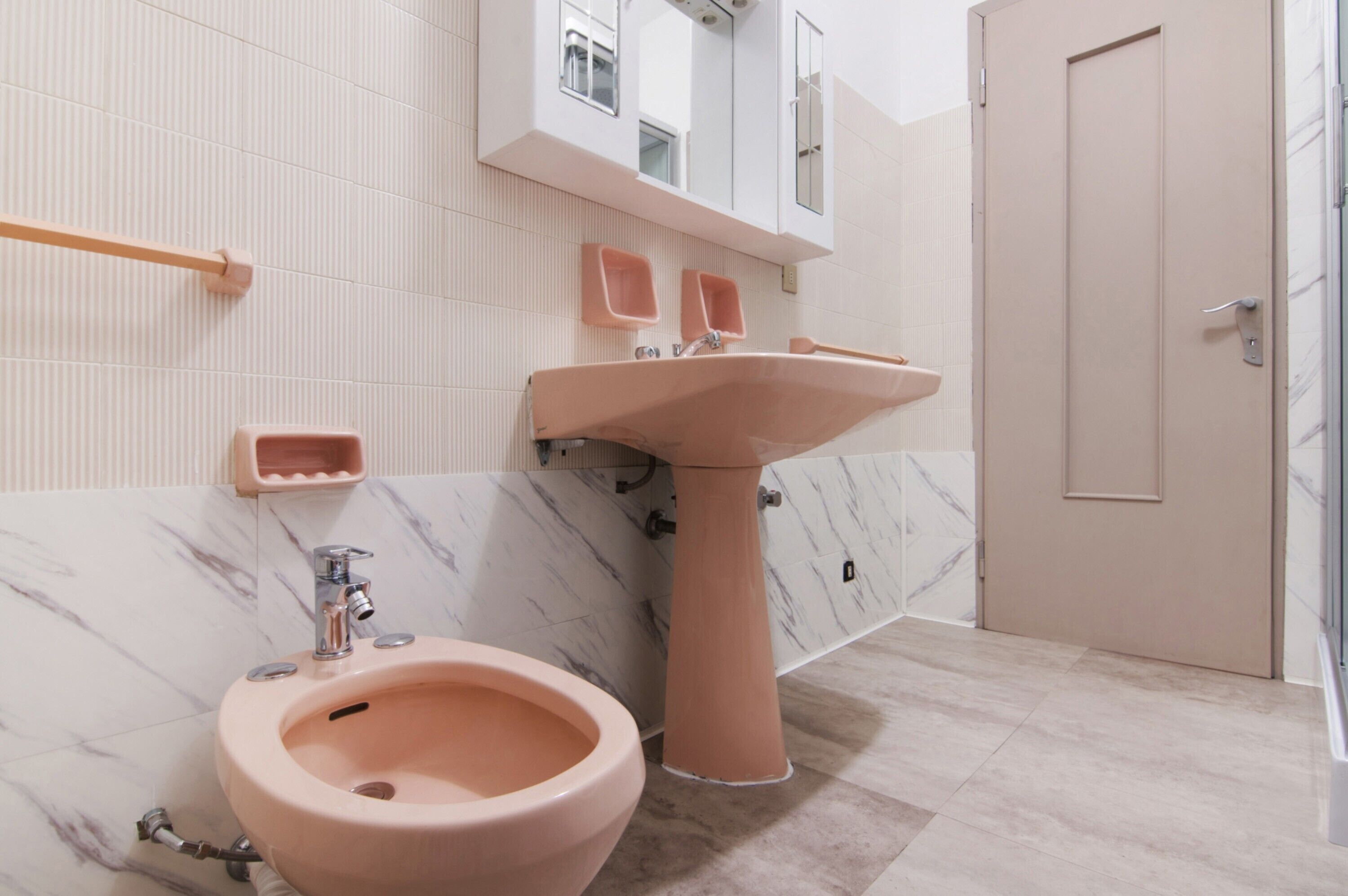 Une salle de bain avec un lavabo rose, un bidet, un miroir et une porte.