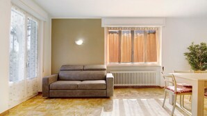 Un salon avec un canapé, une table à manger avec des chaises, un radiateur et une fenêtre avec des rideaux.