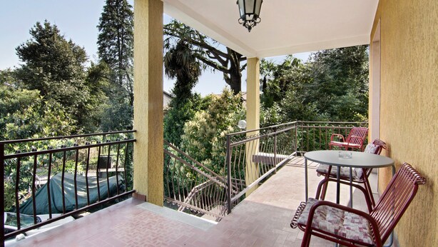 Un balcon avec une balustrade en métal, une table ronde avec des chaises et une vue sur des arbres et une voiture.