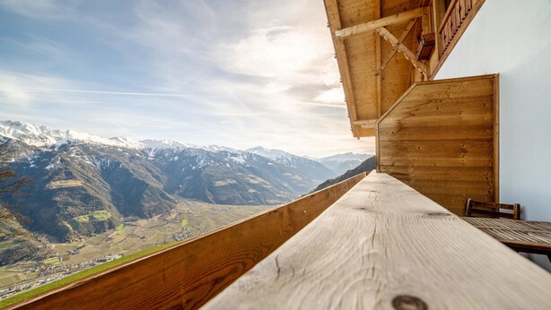 Un balcon en bois offrant une vue sur des montagnes enneigées et une vallée en contrebas.