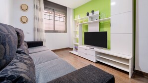 Ein modernes Wohnzimmer mit einer Couch, einem Fernseher auf einem weißen Schrank und einer grünen Akzentwand.