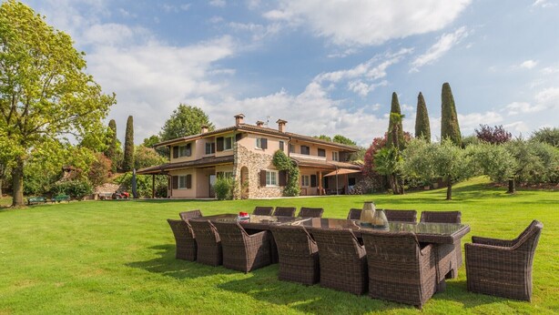 Une grande maison avec une vaste pelouse, du mobilier d’extérieur et de grands arbres.
