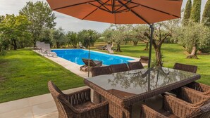 Une piscine avec des chaises longues, une table à manger avec des chaises et un parasol.