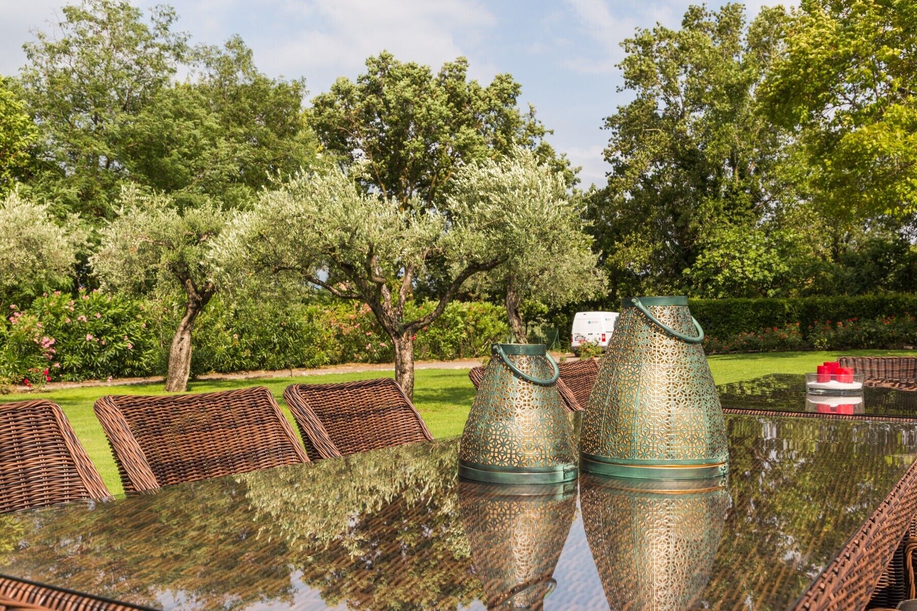 A glass table with wicker chairs and decorative metal lanterns in a garden setting.