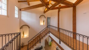 Un escalier en bois avec une rampe en fer forgé, des murs blancs et un plafond avec des poutres apparentes.