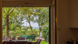 Une vue à travers une fenêtre sur un jardin avec une table et des chaises, un arbre et un banc.